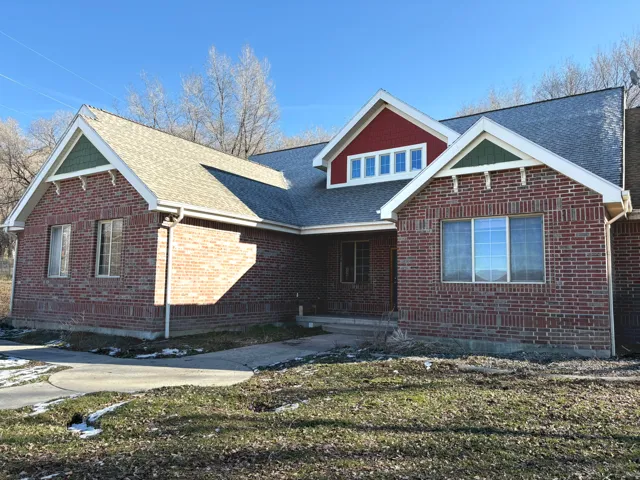 View of front facade with roof with shingles, a front yard, and brick siding