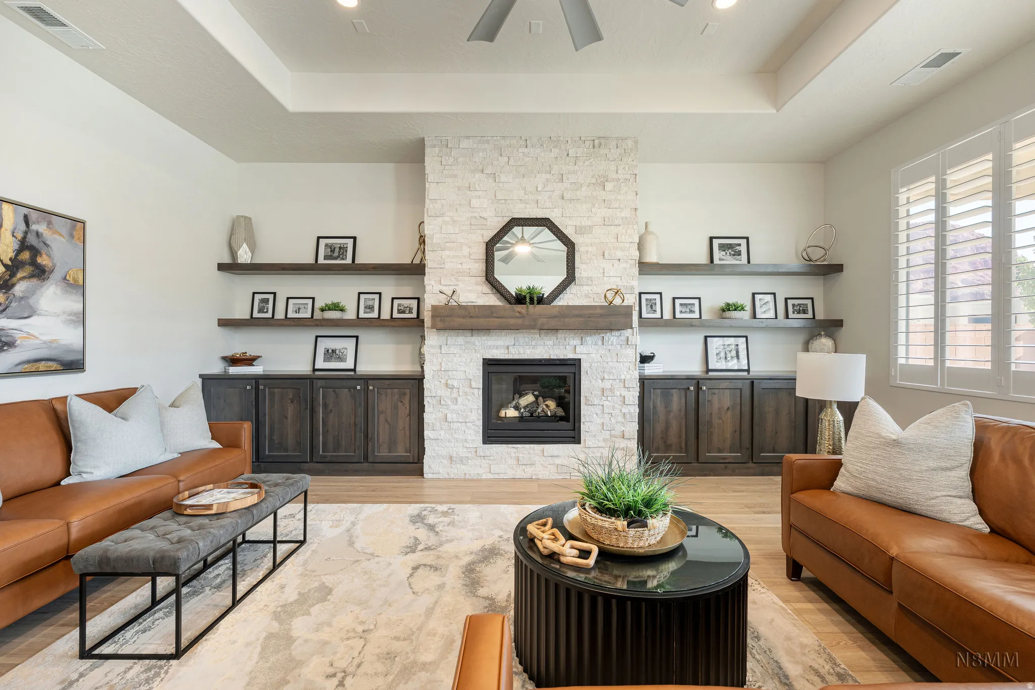 Living room with a tray ceiling, light wood-style flooring, a stone fireplace, and ceiling fan