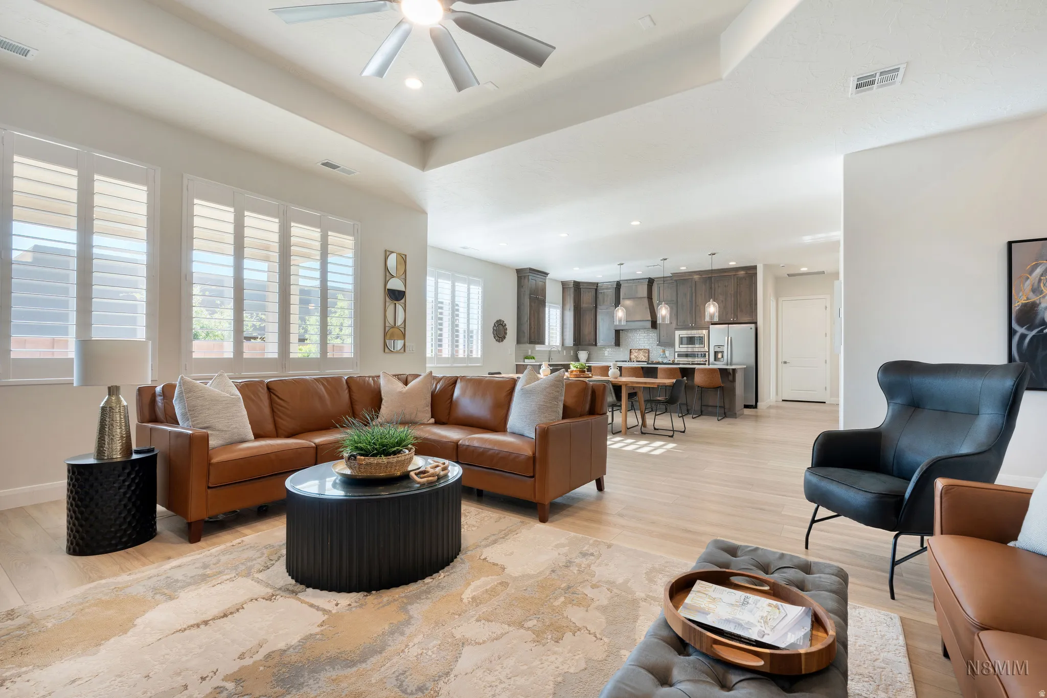 Living room with light wood-type flooring, a tray ceiling, recessed lighting, and a ceiling fan