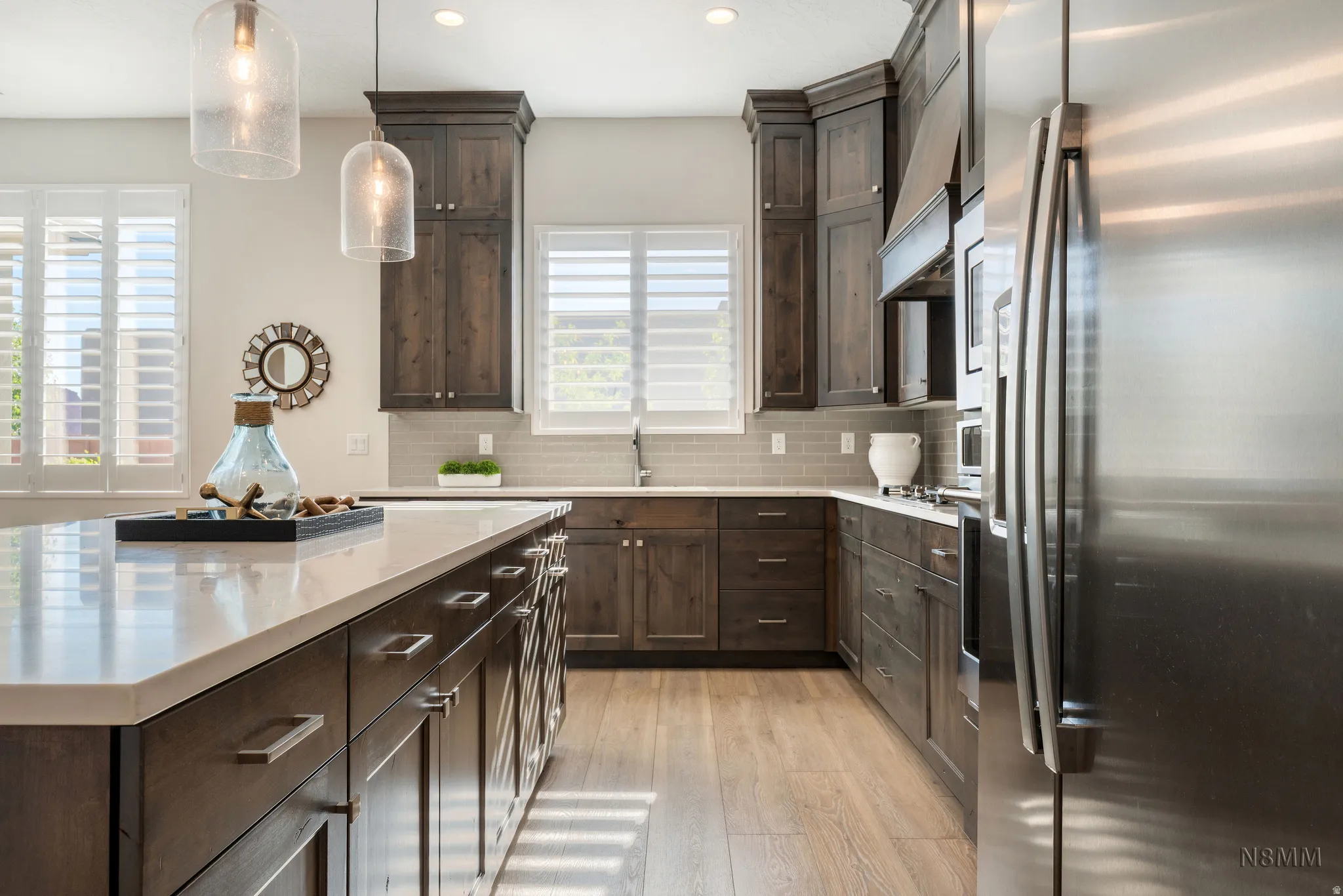 Kitchen with stainless steel fridge with ice dispenser, dark wood finish cabinets, light wood finished floors, hanging light fixtures, and a kitchen island