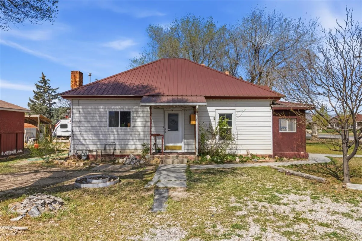 Bungalow-style house featuring a metal roof, a front yard, a chimney, and a fire pit