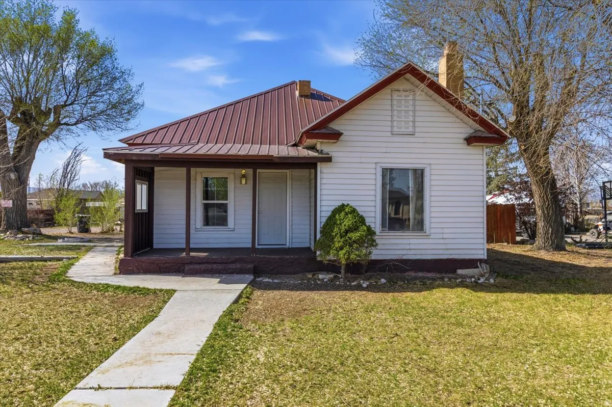 View of front of house featuring covered porch, a front yard, a metal roof, and a chimney