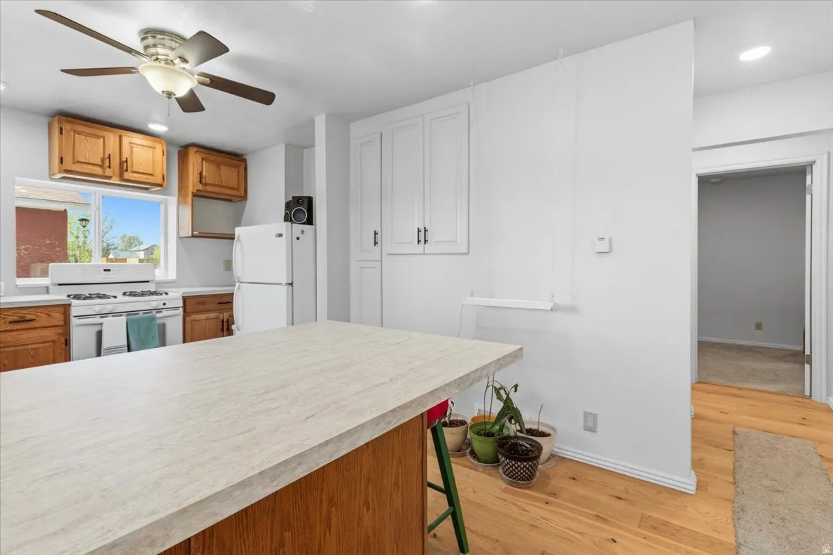 Kitchen with light countertops, recessed lighting, wood finish cabinets, white appliances, and light wood-style floors