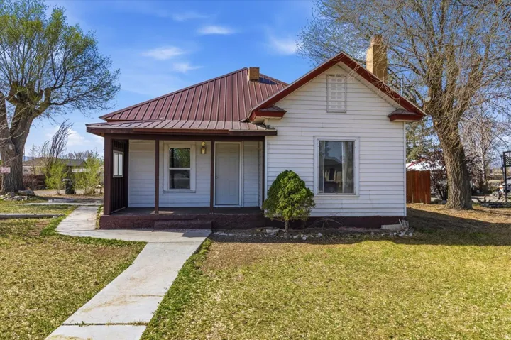 View of front of house featuring covered porch, a front yard, a metal roof, and a chimney