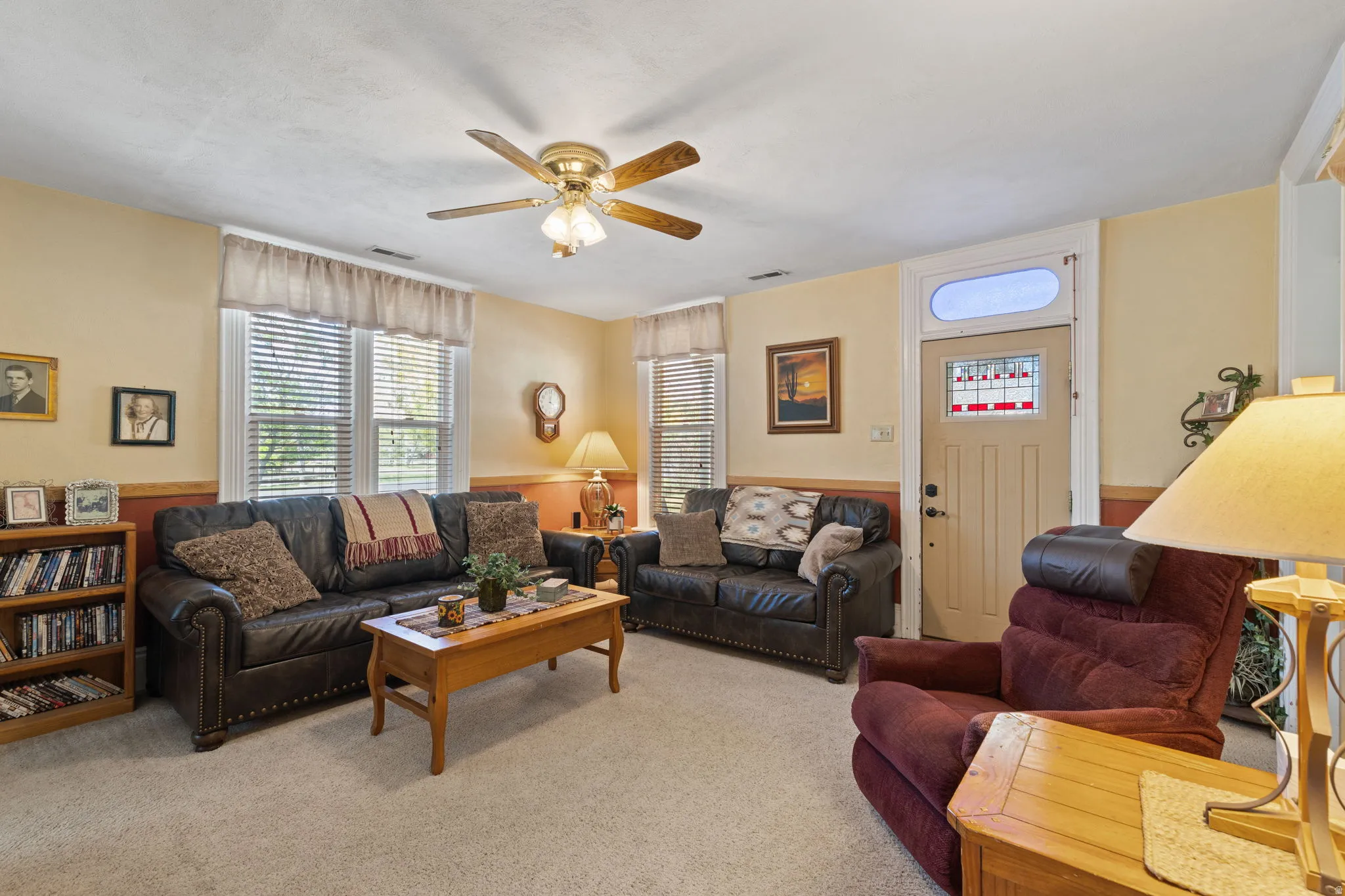 Formal living room featuring light colored carpet, a ceiling fan, and a wainscoted wall