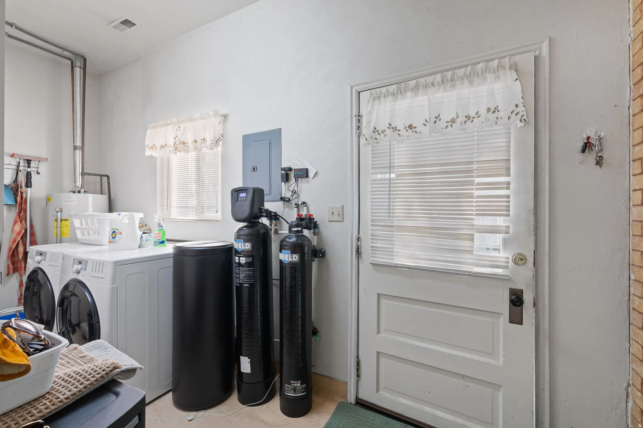 Laundry area featuring electric panel, gas water heater, and washer and dryer and water softener and de-chlorination system