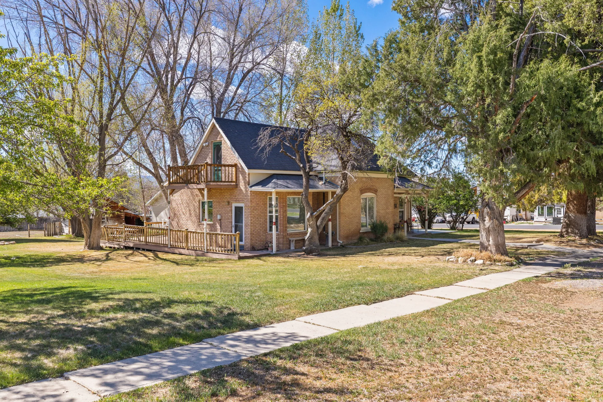 View of front of house featuring a front yard, brick siding, a wooden deck, and a balcony