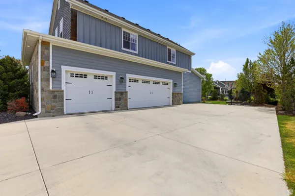 View of side of home featuring board and batten siding, concrete driveway, stone siding, and a garage