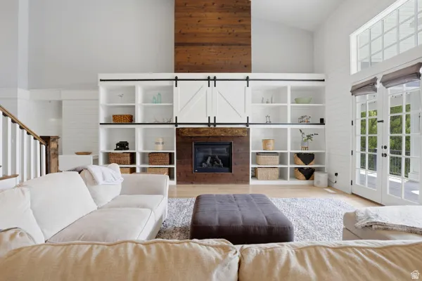 Living area featuring a glass covered fireplace, light wood-style floors, french doors, and vaulted ceiling