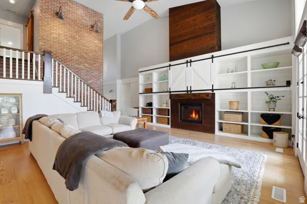 Living area featuring a high ceiling, light wood-style flooring, a glass covered fireplace, a ceiling fan, and a barn door