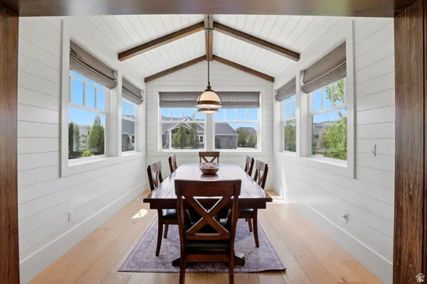 Dining room featuring light wood finished floors, plenty of natural light, beam ceiling, and wooden walls