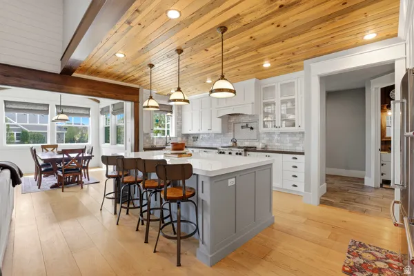 Two tone kitchen with light wood-style floors, decorative light fixtures, a kitchen bar, glass fronted cabinets, and two tone cabinets