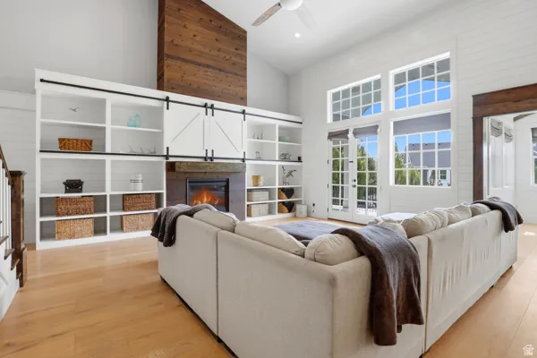 Living area featuring lofted ceiling, a glass covered fireplace, light wood-style flooring, a ceiling fan, and a barn door