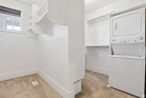 Laundry area featuring light colored carpet and stacked washer / drying machine