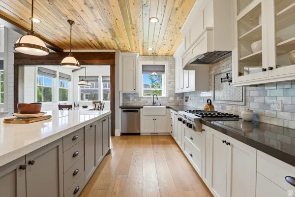 Kitchen with dual tone cabinetry, light wood finished floors, dark stone counters, decorative light fixtures, and stainless steel appliances