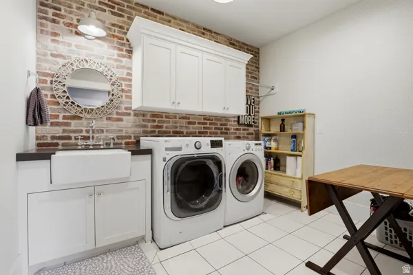 Laundry room featuring washer and dryer, brick wall, cabinet space, and light tile patterned flooring