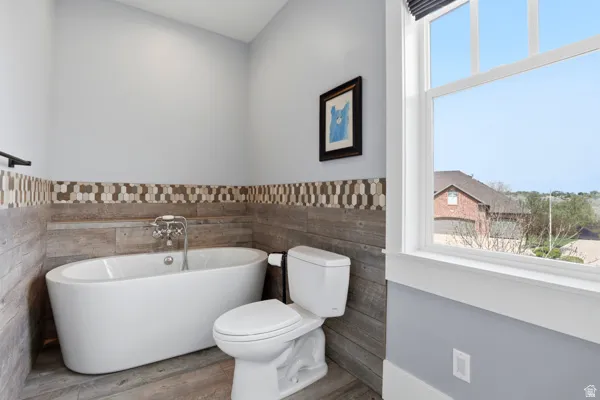 Bathroom with a freestanding bath, wainscoting, wood finished floors, and tile walls