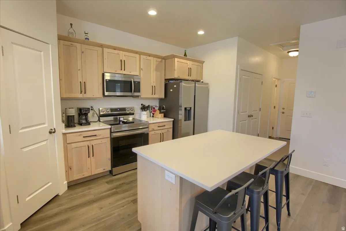 Kitchen with stainless steel appliances, a kitchen island, light wood finish cabinetry, light countertops, and a kitchen breakfast bar