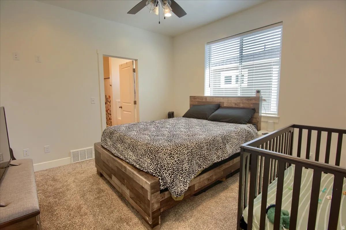 Carpeted bedroom featuring ensuite bath and a ceiling fan