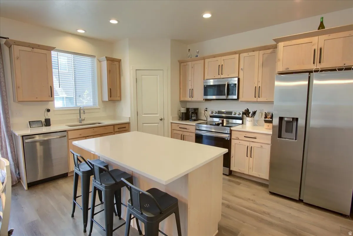 Kitchen featuring stainless steel appliances, light countertops, light wood finish cabinetry, light wood finished floors, and a center island