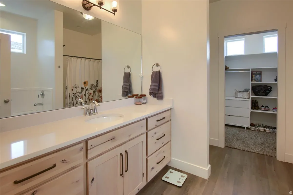 Full bath featuring a spacious closet, vanity, a shower with curtain, and dark wood-style floors