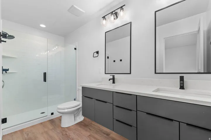 Bathroom with double vanity, a stall shower, light wood finished floors, and recessed lighting