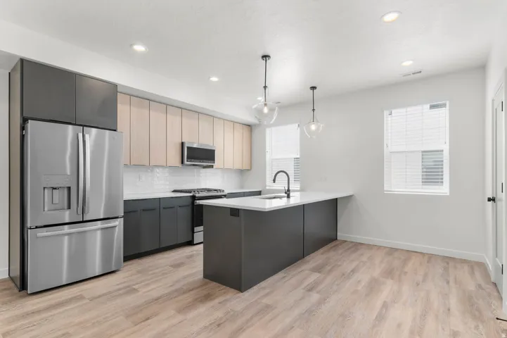 Kitchen with stainless steel appliances, a peninsula, decorative light fixtures, tasteful backsplash, and light wood-style floors
