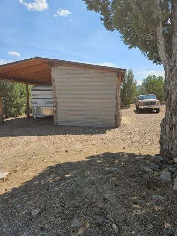Corrugated metal structure with a sloped wooden roof and natural wood support posts, situated on a gravel surface