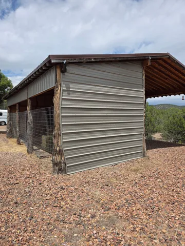 Corrugated metal structure featuring wood posts, an open-sided design, and a sloped roof