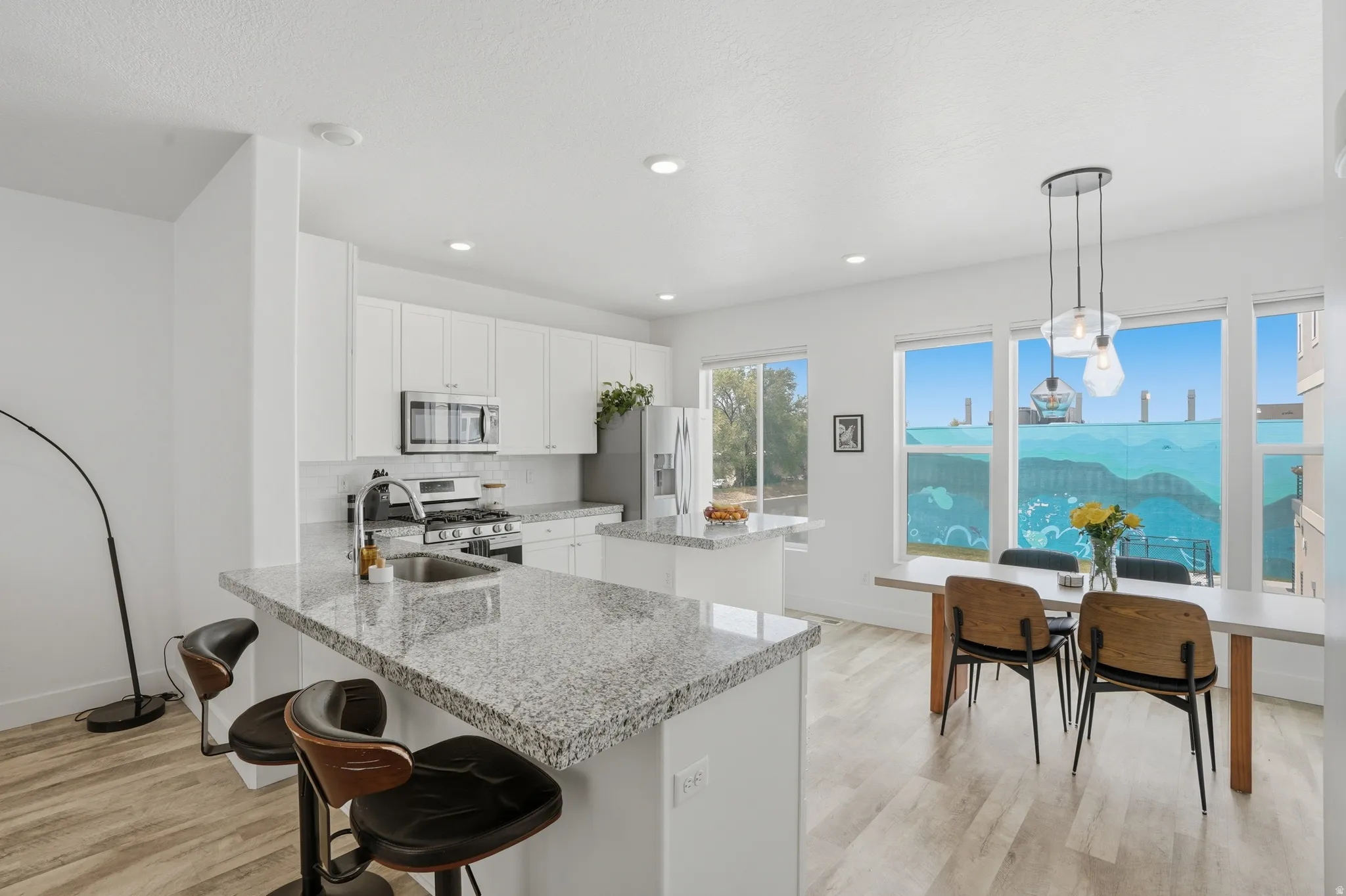 Kitchen with white cabinets, a kitchen breakfast bar, light wood-style flooring, stainless steel appliances, and light stone countertops