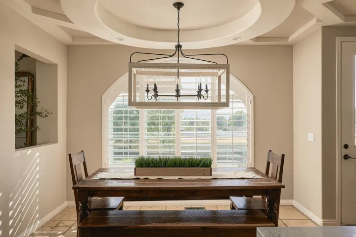 Arched window with plantation shutters, coffered and tray ceiling, and a decorative chandelier