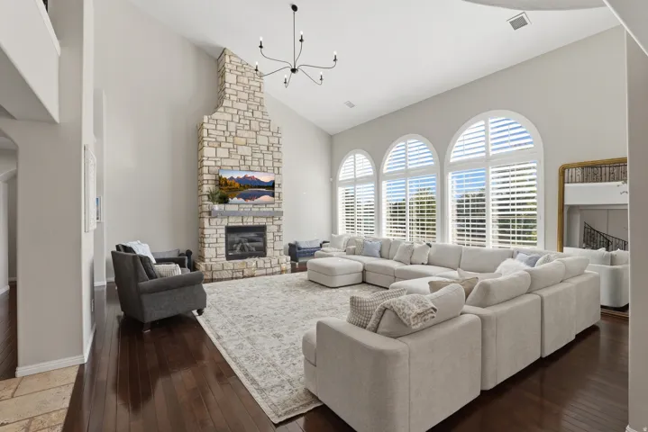 Vaulted ceilings, a full-height stone fireplace, wood-finish flooring, and arched windows with plantation shutters
