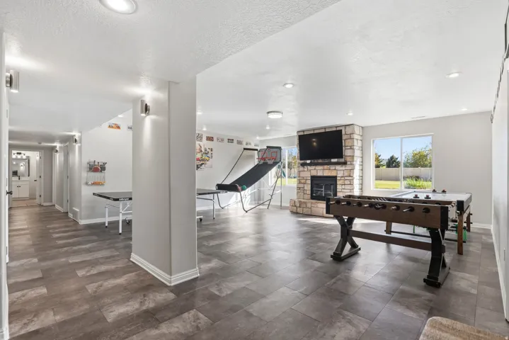Spacious recreation room featuring wood-finish flooring, a stone-clad fireplace, and large windows