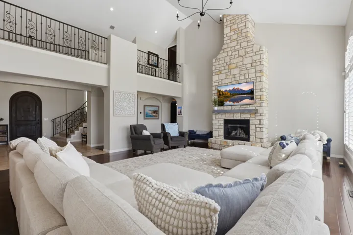 Vaulted ceiling living space featuring a stone-clad fireplace, dark wood-finish flooring, and a wrought iron balcony