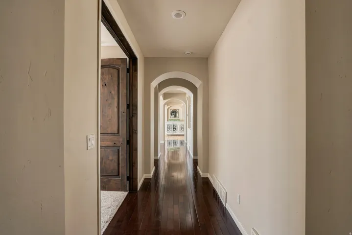 Hallway with dark wood-finish flooring, recessed lighting, arched doorways, and light-toned walls