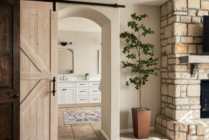 Light wood-finish barn door with black hardware, stone-clad fireplace with built-in mantel, and arched doorway