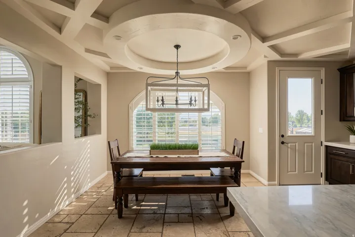 Coffered and tray ceiling features, arched windows with plantation shutters, stone tile flooring, and a glass-paneled exterior door