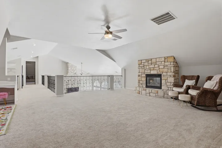 Carpeted loft space featuring an exposed stone-clad fireplace, vaulted ceiling, and decorative metal railing