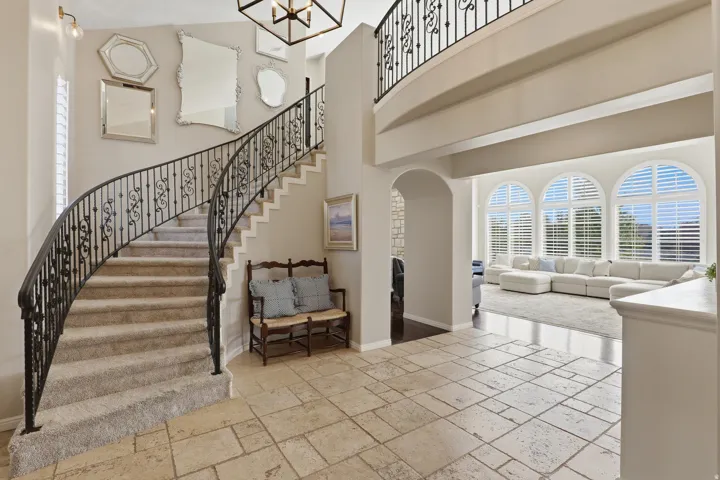 Curved staircase with ornate wrought iron railing, stone-look tile flooring, and arched windows with plantation shutters