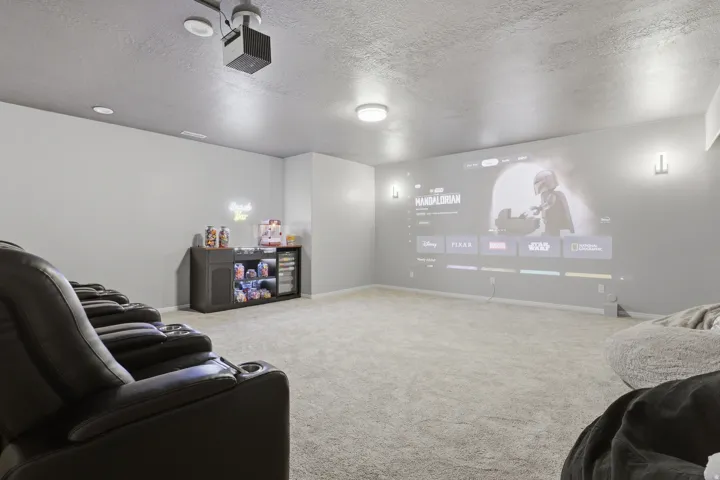 Dedicated media room featuring a ceiling-mounted projector, wall-mounted sconce lighting, and plush carpet flooring