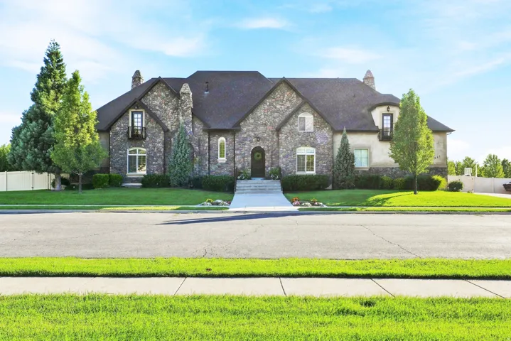 Stone exterior with stucco accents, gabled roofline, mature landscaping, and a concrete pathway leading to the entry