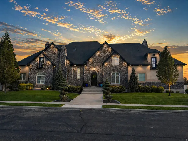French country inspired facade with stone siding, a chimney, a front lawn, and stucco siding