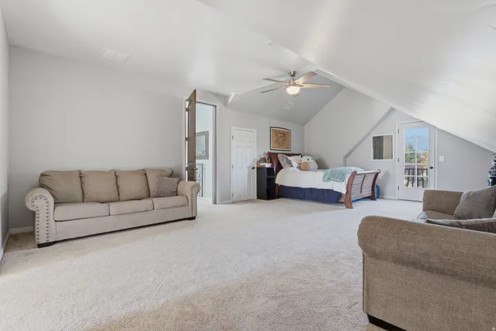 Spacious room with sloped ceilings, light-colored carpeting, a ceiling fan, and a glass-paneled door leading to an exterior balcony