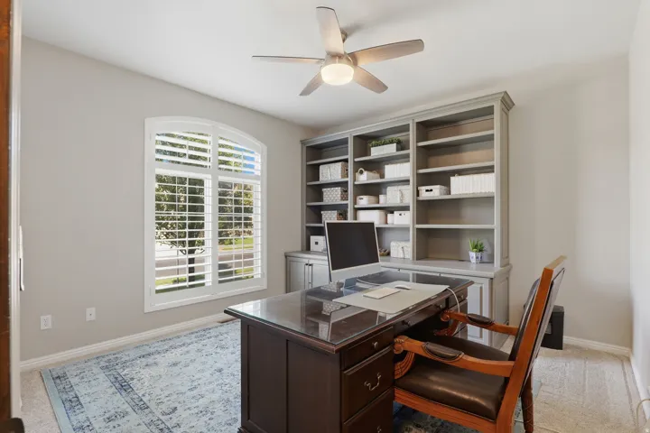 Arched window with plantation shutters, built-in shelving, integrated cabinetry, and ceiling fan with light fixture