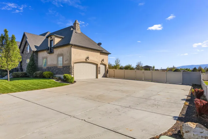 View of side of home with stone siding, stucco siding, driveway, an attached garage, and a chimney