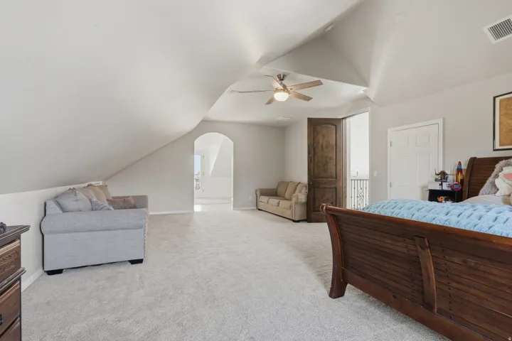 Expansive carpeted room featuring vaulted ceilings, a ceiling fan with integrated lighting, an arched doorway, and a dark wood paneled door