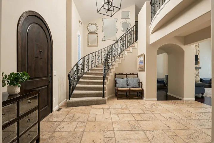 Arched entry door, tile flooring, curved staircase with wrought iron railing, arched doorways, and a tiered chandelier