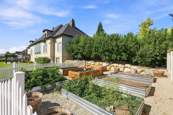 Backyard garden area with multiple raised beds, gravel ground cover, and a white picket fence