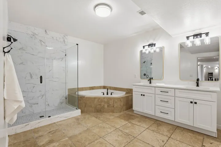 Bathroom featuring double vanity, stone tile floors, a garden tub, and a marble finish shower