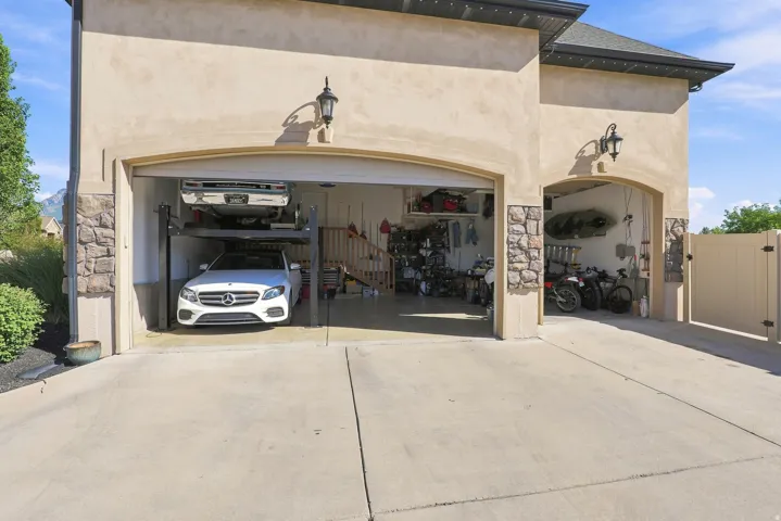Stucco exterior featuring stone accents, an arched garage entry, and a paved driveway